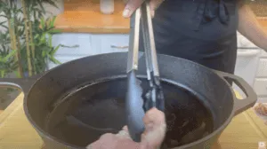 Cooking chicken in a cast iron skillet with tongs, kitchen countertop in the background.